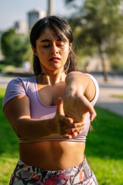 Genç etnik kadın parkta yoga sırasında esneme egzersizi yapıyor.