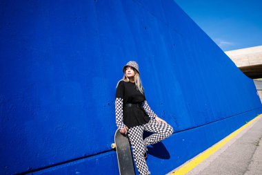 Parlak duvara yaslanmış kaykaylı kendine güvenen bir kadın.