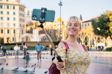 Gülümseyen kadın parkta akıllı telefondan selfie çekiyor.