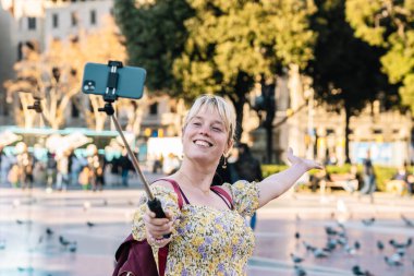 Gülümseyen kadın Barcelona 'nın merkezinde akıllı telefondan selfie çekiyor.