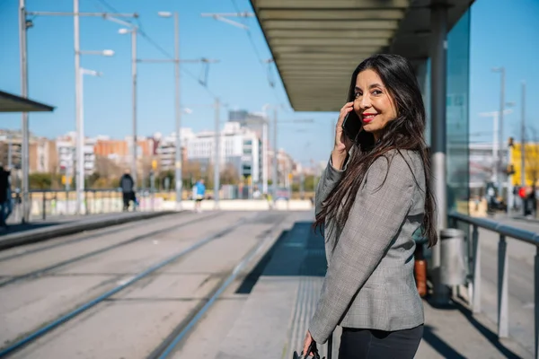 Heureuse élégante femme d'affaires hispanique ayant un appel téléphonique sur la station de tramway — Photo