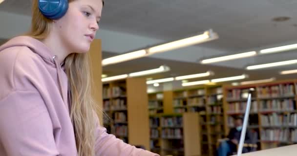 Jovem com laptop e fones de ouvido em uma biblioteca — Vídeo de Stock