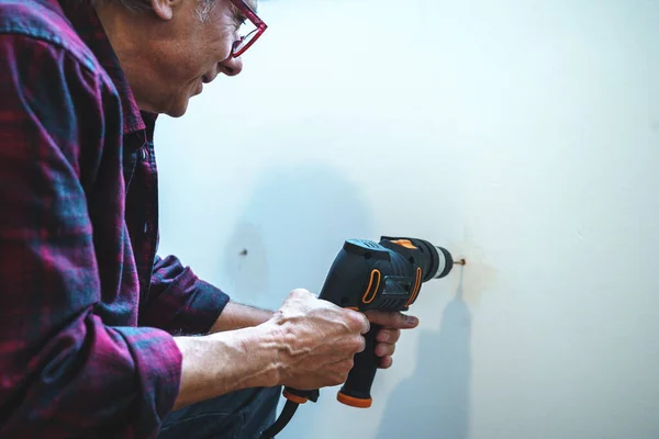 old person using the drill to make a hole in the wall