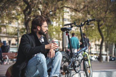  İş adamı bisikletiyle otururken kahve içer. 