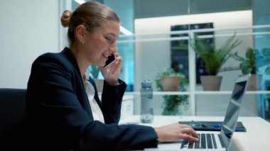 İş kadını dizüstü bilgisayar kullanırken telefonla konuşuyor