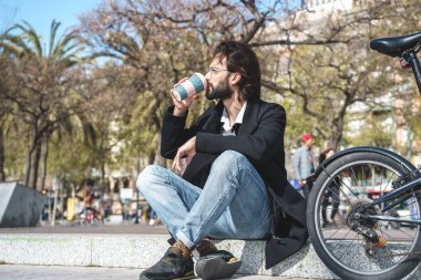 Genç adam bankta oturur ve bir fincan kahve içer.