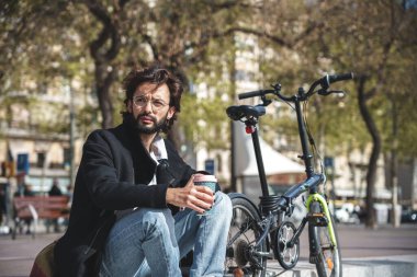 Genç adam bankta oturmuş elinde bir fincan kahve tutuyor.