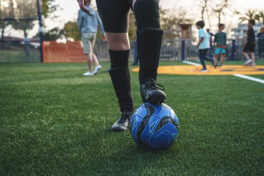 Aktif giyimli ve koruyucu pedli tanınmayan bayan futbolcuların yarışma sırasında çimenli sahada bacakları topun üstünde durmaları.