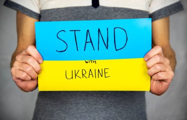 Gri üzerinde duran bir adam, elinde sarı-mavi bir karton Ukrayna bayrağını tutuyor. Üzerinde 