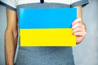 Gri arka planda duran bir adam tek elinde temiz sarı-mavi bir Ukrayna bayrağı tutuyor.