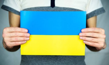 Gri arka planda duran bir adam iki elinde de temiz sarı-mavi bir Ukrayna bayrağı tutuyor. 