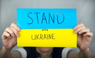 Gri üzerinde duran bir adam, elinde sarı-mavi bir karton Ukrayna bayrağını tutuyor. Üzerinde 