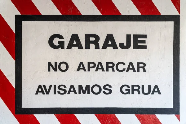 Garage warning sign, no parking, tow truck warning, painted on the wall at the entrance of a garage in Spanish.