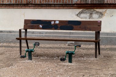 Madrid, İspanya. 18 Mart 2022. Yaşlı insanları eğitmek için önünde pedallar olan ahşap bir bank, bir parkın pis bir alanında..