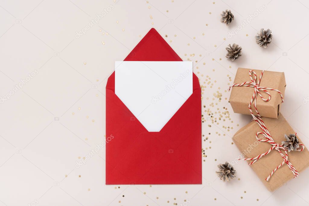 Blank square paper mockup envelope red, golden stars confetti, gift boxes on beige background. Flat lay, top view, copy space, minimalist. Christmas and New Year concept