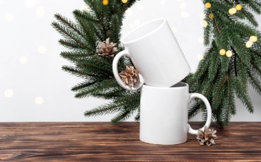 Kahverengi ahşap bir masada iki beyaz çay fincanı ve Noel ağacı çelengi dalları. Tasarımınız için kase şablonu, kopyalama alanı ile logo. Yeni Yıl