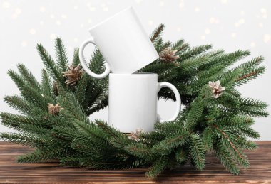 Kahverengi ahşap bir masada iki beyaz çay fincanı ve Noel ağacı çelengi dalları. Tasarımınız için kase şablonu, kopyalama alanı ile logo. Yeni Yıl