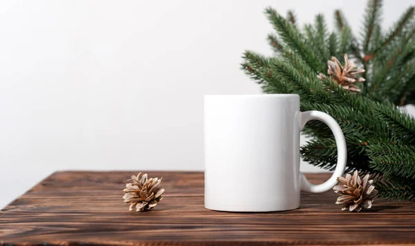 Christmas mockup one white empty tea mugs on a brown wooden table and branches of a Christmas tree wreath. Cup template for your design, logo with copy space. New Year