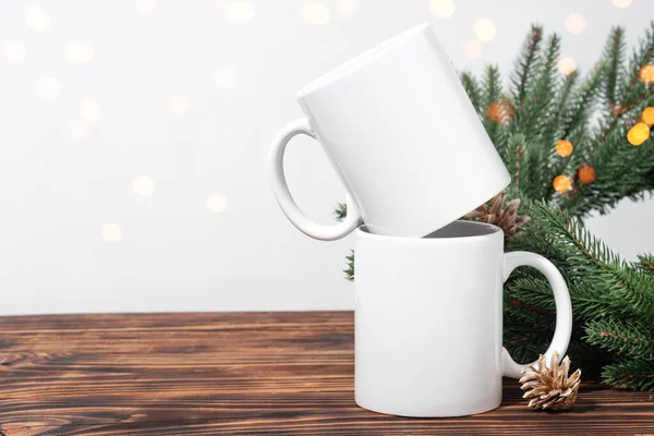 Kahverengi ahşap bir masada iki beyaz çay fincanı ve Noel ağacı çelengi dalları. Tasarımınız için kase şablonu, kopyalama alanı ile logo. Yeni Yıl