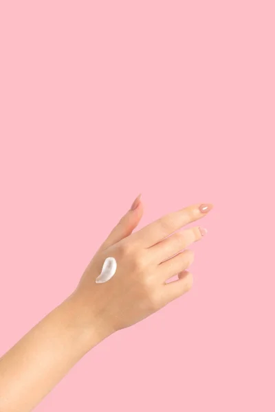 Female hand on a pink background smear cream, long beige nails, manicure and gel polish. Woman taking care of her skin and body