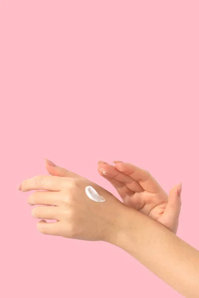Female hands on a pink background smear cream, long beige nails, manicure and gel polish. Woman taking care of her skin and body
