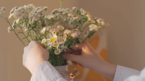 A lány kiegyenesít egy csokor vadvirágot egy vázában az asztalon. — Stock videók