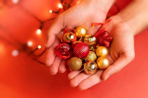 Een man heeft veel rood en goud kerstspeelgoed in handen, een rode achtergrond — Stockfoto