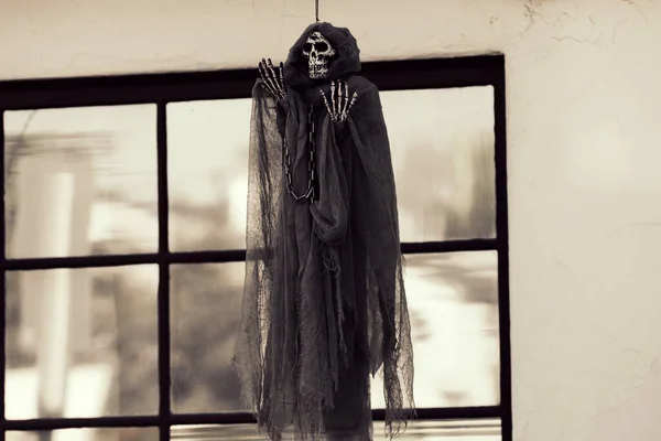 Das Totenskelett hängt am Fenster des Einfamilienhauses. Szenerie für Halloween im Oktober. Dekoration im Hof. — Stockfoto