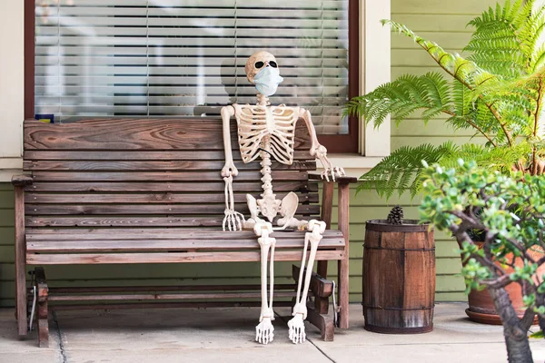 Esqueleto enmascarado en el banco, pandemia de coronavirus. Paisaje para Halloween en octubre. Decoración en el patio. — Foto de Stock