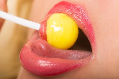 Lolipop emen güzel bir kadının güzel portresini yakından çek. Dudakları pembe rujlu seksi kadın dudakları ağzında leziz yuvarlak kırmızı ve sarı lolipop şekeri çubukta..