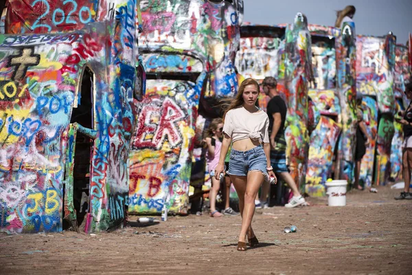 Amarillo, Texas, USA - 2020: Beautiful young girl blonde with street art spray paint supplies. Young artist and creativity. Youth, leisure. Cadillac Ranch public art installation and car sculpture