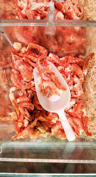 Frozen pink shrimp on ice at the supermarket or fish store. Raw seafood in close-up. Fresh frozen shrimp, deli, seafood concept, close-up. Vertical photo format.