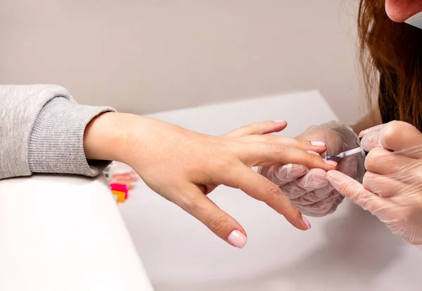 Master applies a decorative light pink gel nail polish with a brush. The concept of beauty and nail care