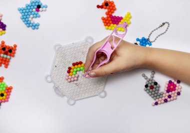 Handmade with childrens hands, handmade aqua mosaic on the table, selective focus. Childrens educational game aqua mosaic, inserts multicolored beads into the pattern with a special pen