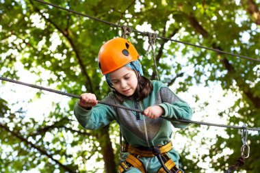 Portrait of cute little beautiful girl walking on a rope bridge in an adventure rope park