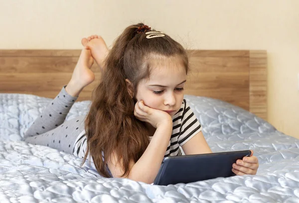 Girl laying on bed and using tablet. Watching videos, online training. quarantine. Concept of internet, social media, online and technology impact to children life