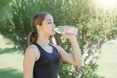 Genç bir kız şeffaf plastik şişeden su içiyor..