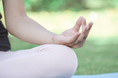 Kız yeşil bir şehir parkında lotus pozisyonunda oturuyor. Kızın vücudunun bir parçası..