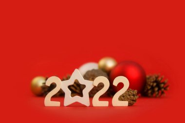 İçinde 2022 numara olan Noel kartı, yeni yıl baloları, kırmızı arka planda köknar konileri. Şenlik düzeninin temeli. Yan görünüm.