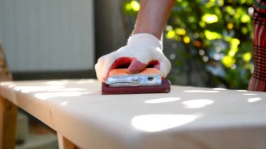 Koruyucu eldivenli erkek ellerinin yakın çekimi dışarıda yeni bir ahşap tahta öğütüyor. İnşaat talaşından elde edilen güzel toz güneş ışığı ışınlarında işliyor. Boşluğu kopyala