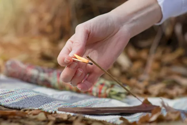 女性の手は暖かい秋の日に香棒に火をセットします 屋外リラクゼーション演習のために設定 — ストック写真