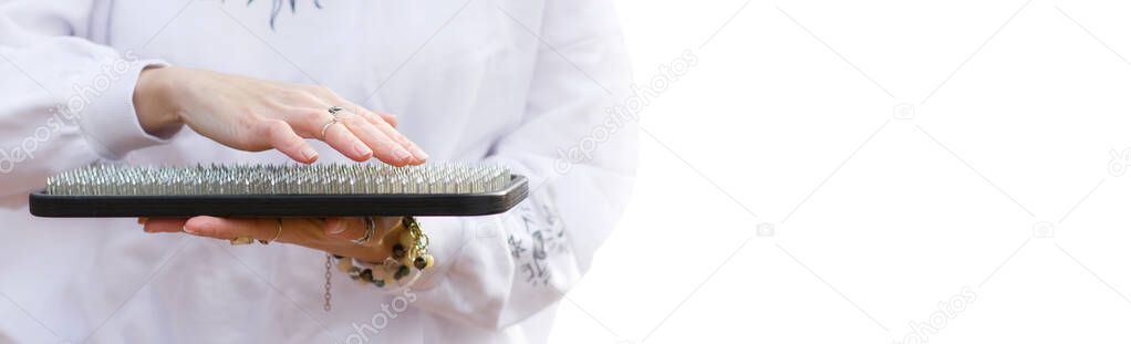 Close-up of female hands holding a sadhu board on a white background. Banner. A girl in a white sweater holds a board with sharp nails for yoga and meditation. Place for text