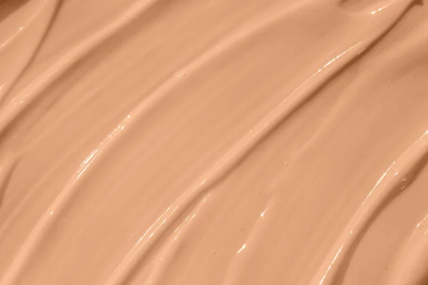 Make up base, cream textured background. Beige nude liquid foundation texture, concealer smear smudge drop. Closeup macro. Cosmetic tonal makeup moisturizer