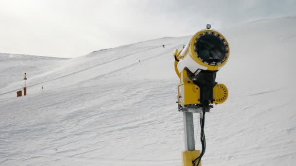 Livigno, Włochy - 21 lutego 2022: Maszyna do produkcji śniegu, armata śnieżna w ośrodku narciarskim Livigno, Włochy w słoneczny zimowy dzień i narciarze w tle. 4k materiał wideo — Wideo stockowe