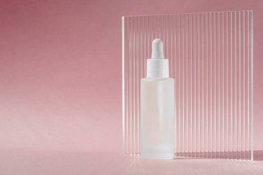 Kolajenle serum yağı ve şeffaf beyaz şişede peptit. Pembe arka planda damlatıcı ve akrilik kabartmalı çarşaf. Cilt bakımı cilt modeli sıvı kozmetik ürünü.