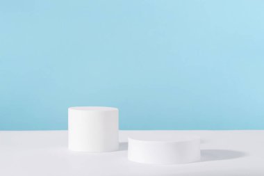 Mavi arka planda kozmetik ürün ambalajı için podyum kaidesi. Mücevher sunumu için vitrin, parfüm reklamı için beyaz platform, kozmetik standı, markalaşma sahnesi
