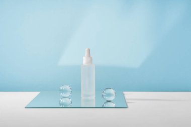 Peptidli serum kozmetik şişesi ve aynada retinol mavi arka planda cam toplar. Hyaluronik asit kozmetik ürünleri şık malzemelerle paketleme yapıyor. Serum güzellik düşürücü