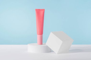 Maket kürsünün mavi arka planında kozmetik krem pembe şişe maketi. Markasız losyon güzellik ürünü ambalajı. Ürün sunumu taklit ediliyor. Losyon, temizleyici, cilt bakımı için şampuan.