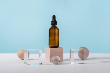 Yağ kozmetik kehribar ürün ambalajı ve şık dekorlar. Mavi arka planda peptit ve retinol içeren serum kozmetik şişesi ve ahşap bloklar. Kalıpta serum düşürücü maketi