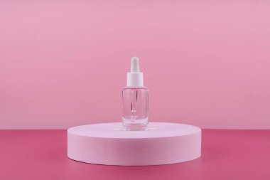Pembe arka plandaki platform kaidesinde peptit ve retinol içeren serum kozmetik şişesi. Hyaluronik asit kozmetik şeffaf moda ürünleri paketleme ve şık aksesuarlar. Serum güzellik düşürücü